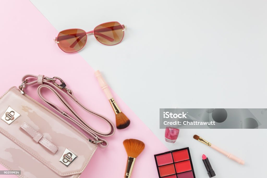 Table top view accessory of clothing women  plan to travel in holiday background concept.Hand bag with many essential  items cosmetic and sun glasses on modern white & pink paper.Duo with pastel tone. Personal Accessory Stock Photo