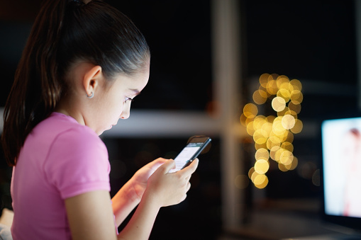 Young people and youth problems. Preteen girl left alone at home, sends text messages with phone to friends. Concept of potential victim of cyber bulling and absence of parental control