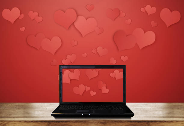 Computer laptop on wooden desk with floating hearts on red background