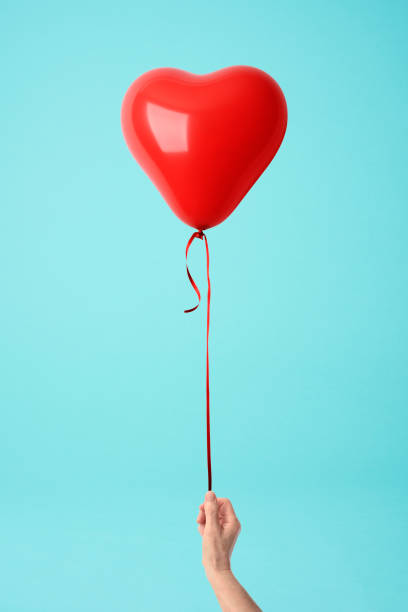 istock Holding a red heart shape balloon against blue background 903149968