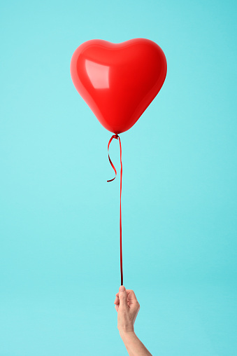 Close-up of holding a red heart shape balloon against blue background.