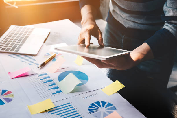 istock business man holding  digital tablet and use laptop to working document accountant analyze income & budget & tax is are planning a marketing plan to improve the quality of their sales in the future. 903160968
