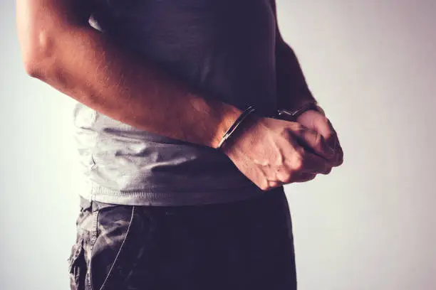 Handcuffed soldier in military army clothes. Prisoner of war or arrested terrorist, close up of hands in handcuffs, selective focus.