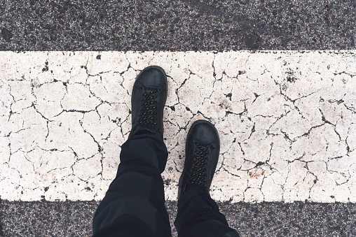 Man on pedestrian zebra street crossing, overhead view of male feet in black boots on asphalt road