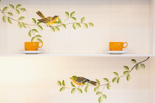 Yellow ceramic cups on a white wood cupboard painted with birds and leaves