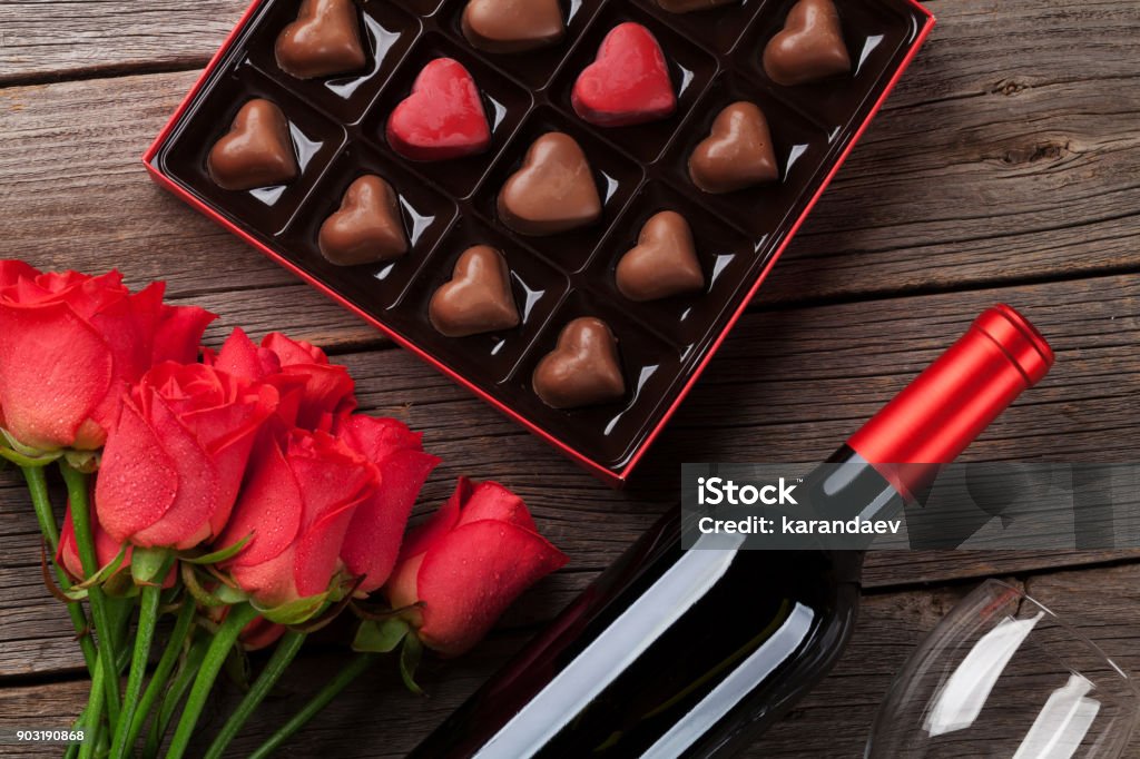 Valentines day with red roses, wine and chocolate Valentines day with red roses, wine bottle and chocolate box on wooden table. Top view Valentine's Day - Holiday Stock Photo