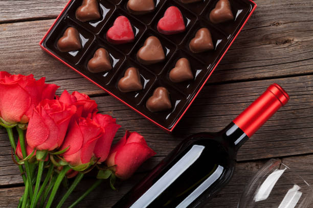 Valentines day with red roses, wine and chocolate Valentines day with red roses, wine bottle and chocolate box on wooden table. Top view wine bottle photos stock pictures, royalty-free photos & images