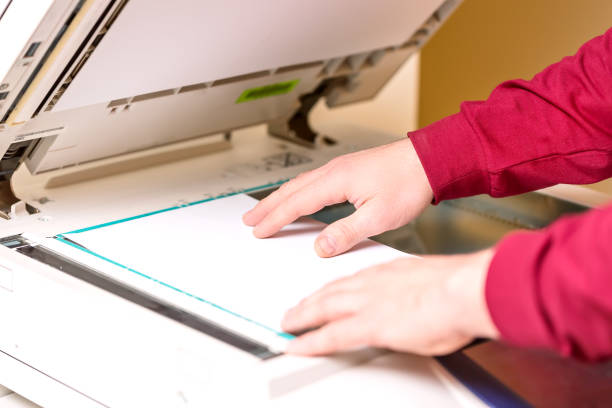 istock Man putting paper sheet on printer for scanning. Office work concept. 903206566