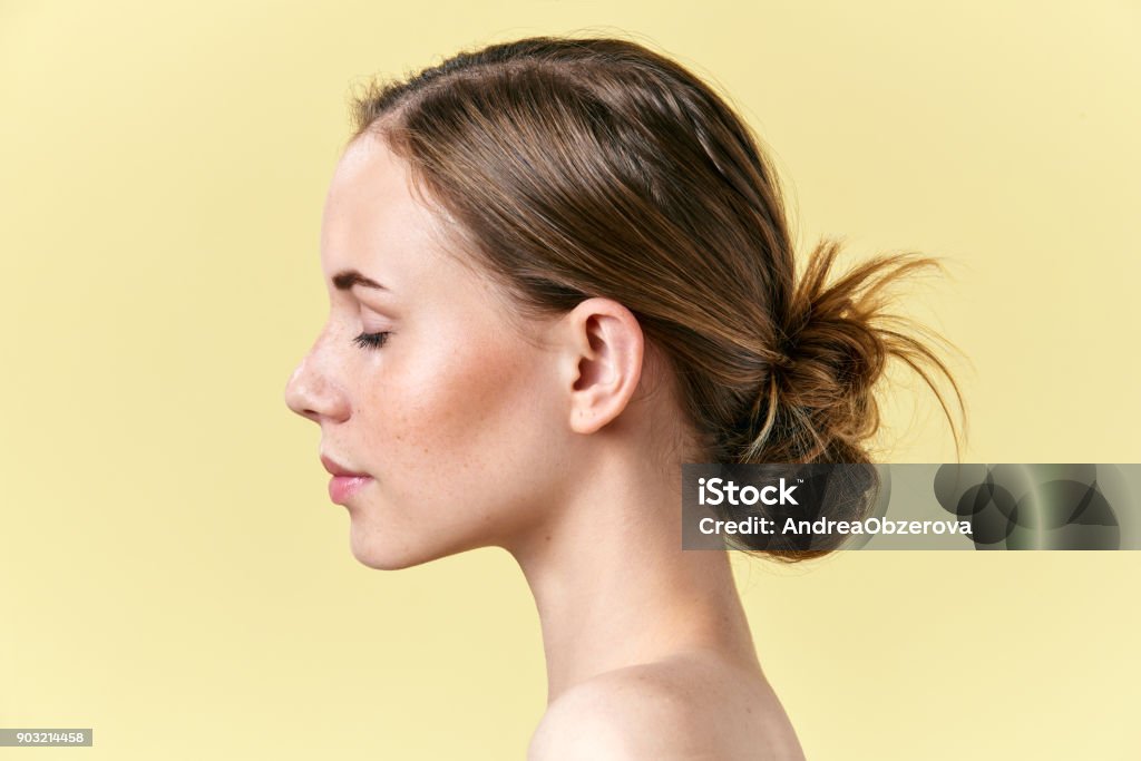 Beautiful redhead woman with freckles studio profile portrait. Model with light nude make-up, closed eyes, isolated on pastel yellow background Skin Stock Photo