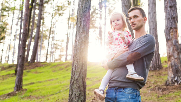 istock Young father holding cute toddler daughter in his arm while on a walk in a forest, both looking into distance. 903233940