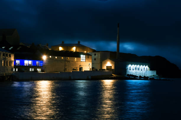 Bowmore Distillery at night, Islay, Scotland Bowmore Distillery and its bonded warehouses after sunset on the coastline of the island of Islay, Scotland. Located at the island's main village of Bowmore, it is one of eight (soon to be at least ten) distilleries on the island producing whisky with a peaty taste. bowmore whisky stock pictures, royalty-free photos & images