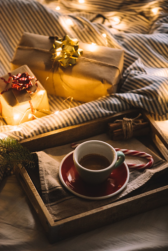 Fancy morning with presents in bed: presents wrapped in bright paper, fireflies and a fresh  morning coffee in a ceramic cup with a saucer in a wooden tray on a bed background