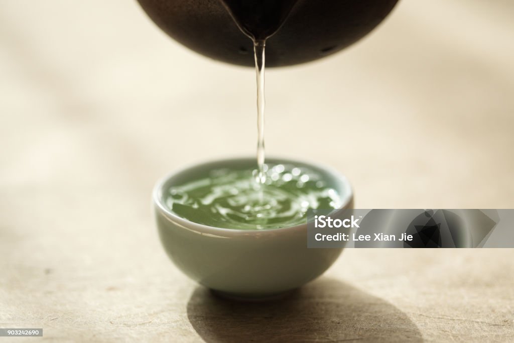 Sencha being poured into a celadon teacup Japanese sencha, green tea, pours into a small celadon porcelain teacup resting on a washi paper background. Green Tea Stock Photo