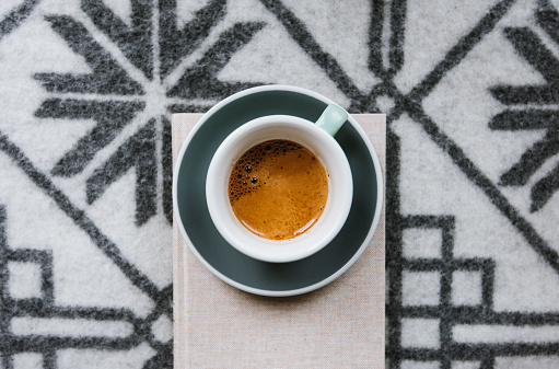 Delicious fresh strong morning espresso coffee with a beautiful tiger crema in a thick ceramic cup with a saucer on the comfy wool blanket background, flat lay