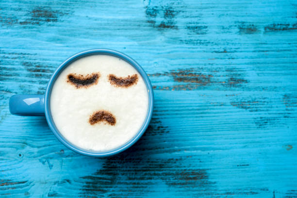 cup of cappuccino with a sad face high-angle shot of a blue cup of cappuccino with a sad face drawn with cocoa powder on its milk foam, on a blue rustic table with a blank space on the right bad coffee stock pictures, royalty-free photos & images