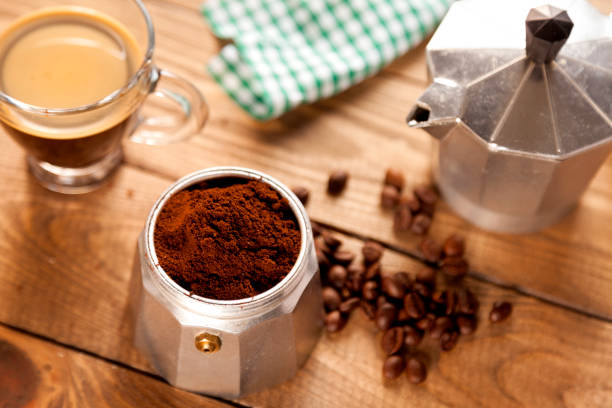 Italian coffee maker, napkin, cup of coffee and coffee beans on wood table