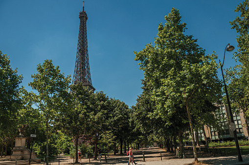 Paris, France - July 07, 2017. People, greenery and Eiffel Tower with sunny blue sky in Paris. Known as the “City of Light”, is one of the most awesome world’s cultural center. Northern France.