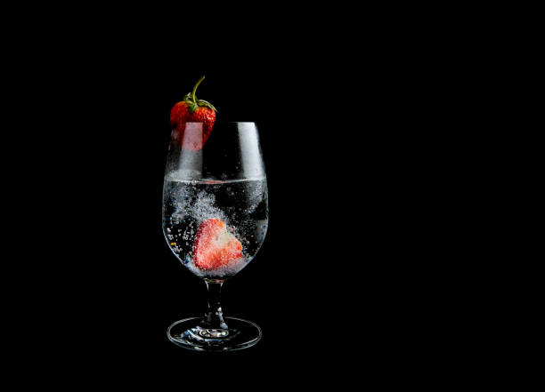 Sparkling water with strawberry in a high glass on black background.