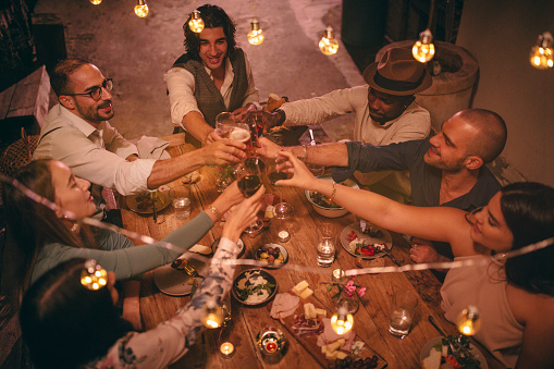 Young multi-ethnic friends celebrating and toasting at rustic dinner party