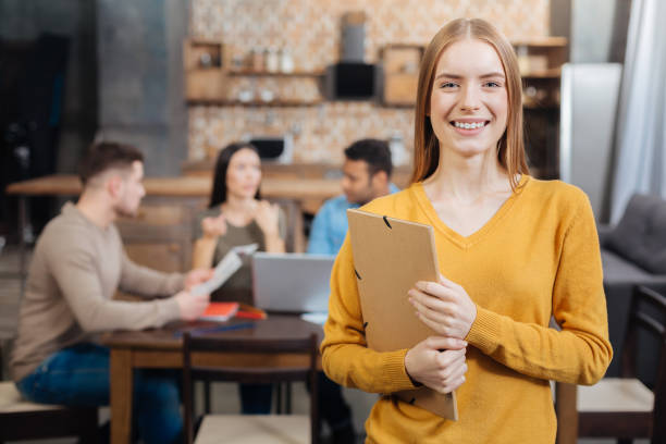 istock Cheerful young woman holding a folder and smiling while her colleagues working 903277840
