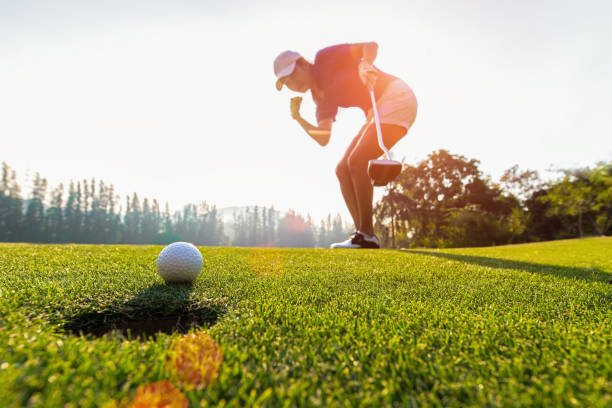 asiatische frau golfer gewinnt nach langen putt golfball am grünen golf, sonnenuntergang, textfreiraum aktion.  gesundes konzept - einlochen stock-fotos und bilder