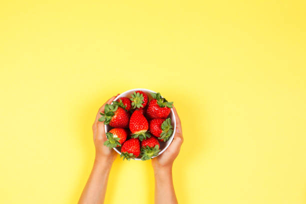 istock Kid holds in hand bowl with fresh strawberries on yellow background 903287208