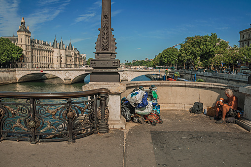 Paris, France - July 08, 2017. Beggar on bridge over the Seine River with sunny blue sky in Paris. Known as the “City of Light”, is one of the most impressive world’s cultural center. Northern France.