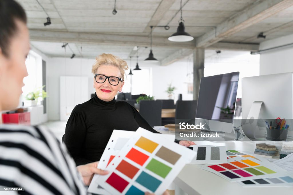 Senior and young interior designers working together in the office Senior interior designer working together with young woman in the office, sitting at the desk and watching color samples. Color Swatch Stock Photo