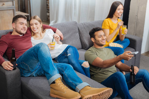 istock Smiling student looking at boyfriend while watching TV with him and friends 903299112