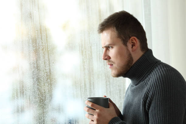 istock Angry man looking through a window in a rainy day 903309582