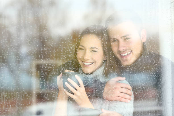 позитивная пара, смотря в окно дождливый день - window rain winter house стоковые фото и изображения