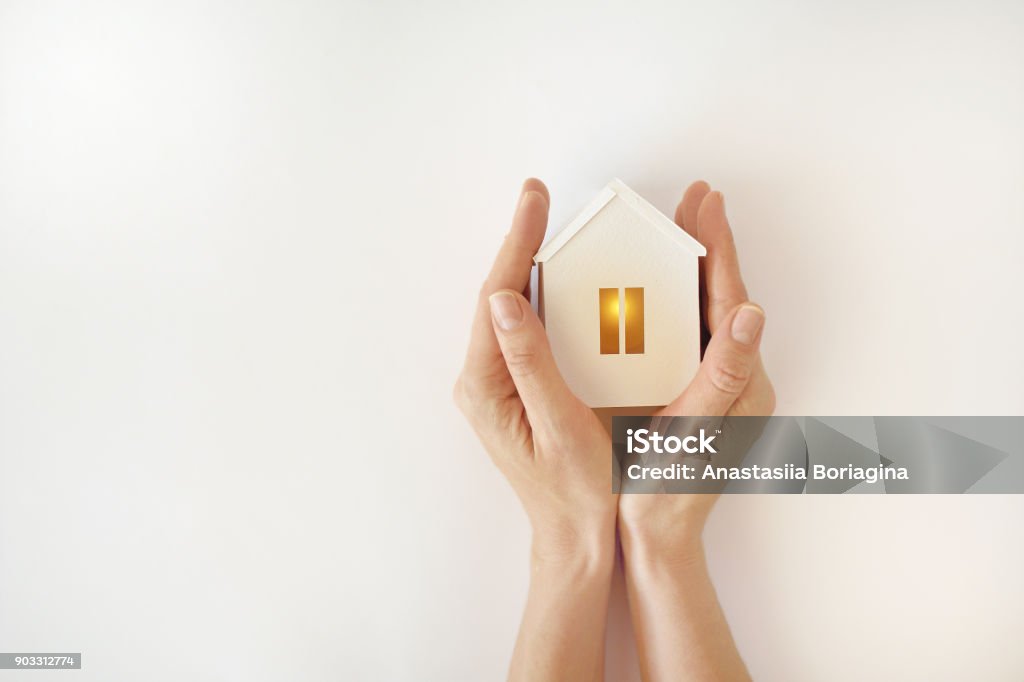 O modelo da casa branca com luz quente dentro nas mãos femininas em um fundo branco - Foto de stock de Casa royalty-free