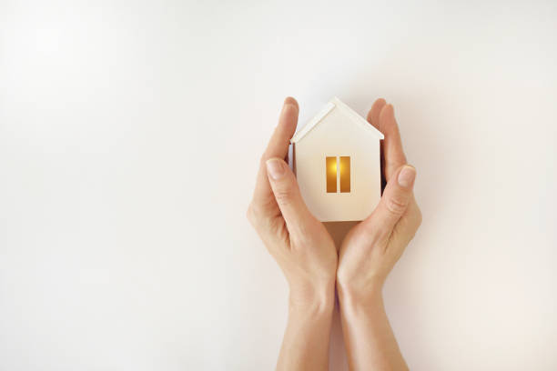 модель белого дома с теплым светом внутри в женских руках на белом фоне - household insurance стоковые фото и изображения