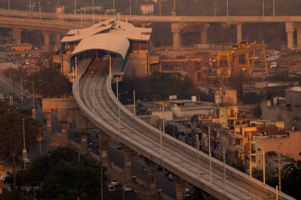 Under construction overhead metro line and station Under construction metro line and station shot at dusk. The golden light and foggy atmosphere of noida delhi highlights the residences and offies around the station delhi metro stock pictures, royalty-free photos & images