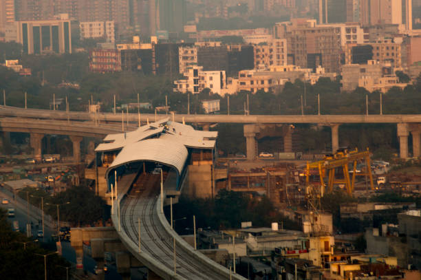 Under construction overhead metro line and station Under construction metro line and station shot at dusk. The golden light and foggy atmosphere of noida delhi highlights the residences and offies around the station delhi metro stock pictures, royalty-free photos & images