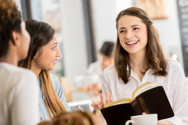 Young adults smile while reading and discussing the Bible together while at a coffee shop.