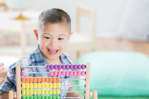 An excited little boy with Down syndrome uses an abacus.