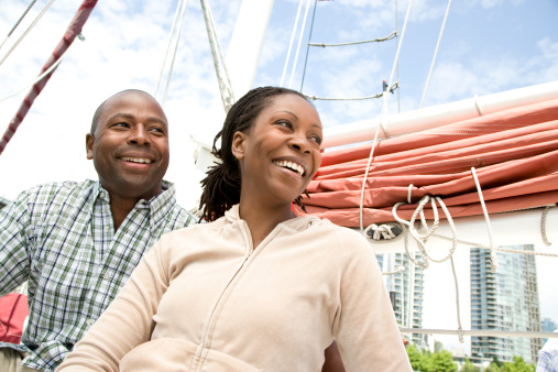 Couple sitting on a boat smiling and gazing ahead. Buildings in background.