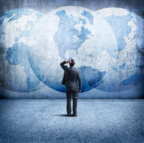 istock Businessman Stands And Looks Up At Three Interlocking Globes On Wall 903369038