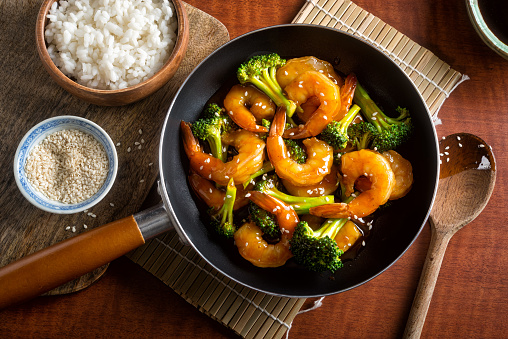 A delicious shrimp teriyaki stir fry with broccoli and sesame seeds on a wooden table top.