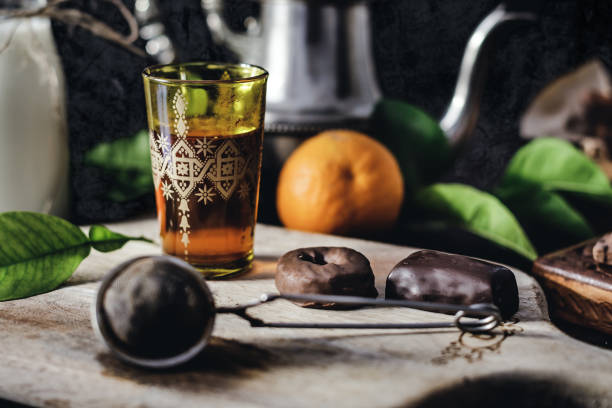 Tea with orange in oriental glass. Milk in glass jar and chocolate sweets. Dark wall at background, selective focus,copy space.