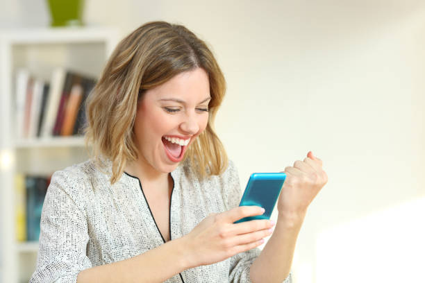Excited woman reading smart phone content Excited woman reading online smart phone content at home playing alone stock pictures, royalty-free photos & images