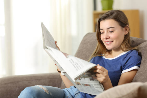 istock Teen reading a newspaper on a sofa at home 903394992