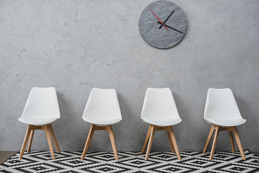 Row of empty white chairs in a waiting room at company with wall clock