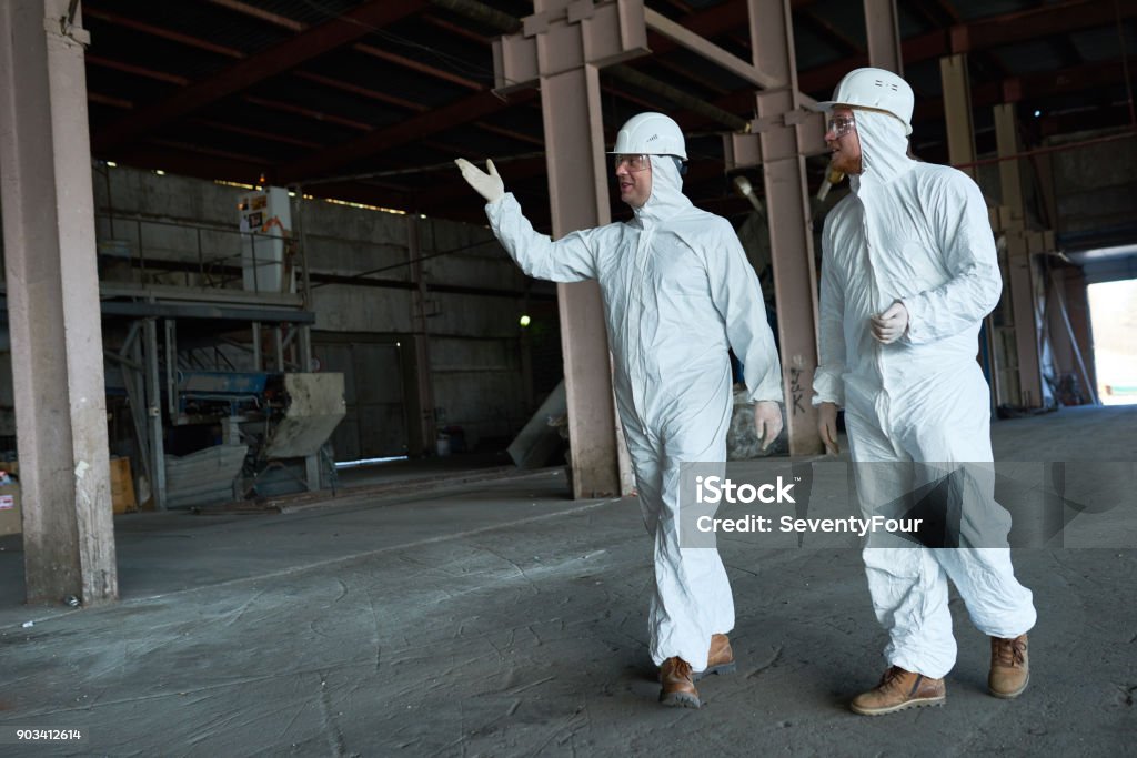 Workers in Protective Suits Crossing Workshop at Modern Factory Full length portrait of two workers wearing biohazard suits walking in industrial warehouse of modern  plant,  copy space Clean Suit Stock Photo