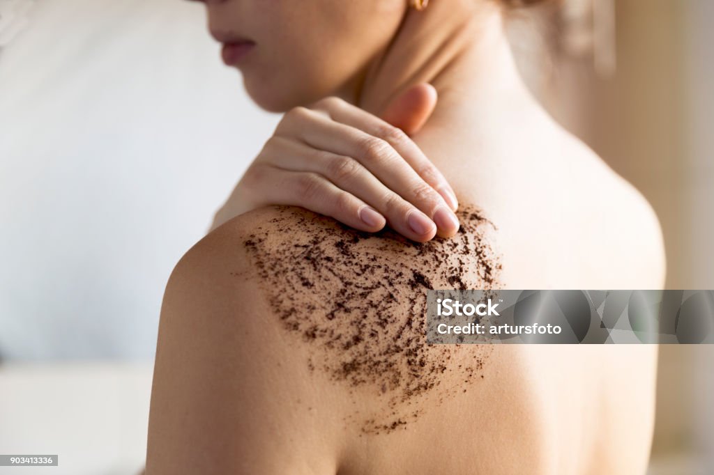 Beauty, spa and healthy skin concept - woman cleans skin of the body with coffee scrub in bathroom. Exfoliation Stock Photo