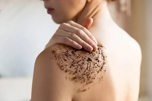 Beauty, spa and healthy skin concept - woman cleans skin of the body with coffee scrub in bathroom.