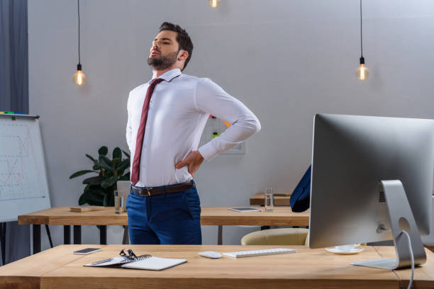 istock tired businessman standing and stretching in office 903414918