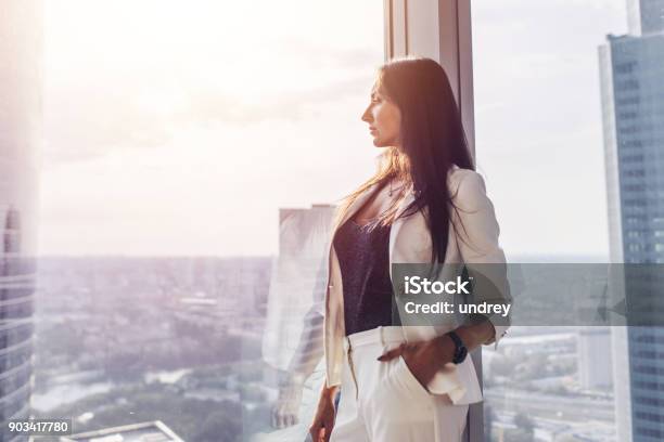 Retrato De Dama Elegante Negocio Usar Traje Formal Blanco De Pie Junto A La Ventana Mirando El Paisaje Urbano Foto de stock y más banco de imágenes de Mujeres