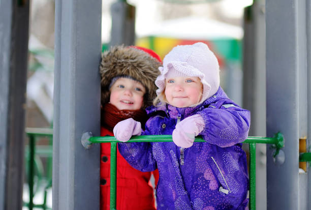 menino e uma menina em roupas de inverno se divertindo no parque infantil ao ar livre - playground snow winter little girls - fotografias e filmes do acervo